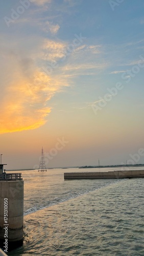 Sunset over the water with a sailboat in the distance and clouds in the sky