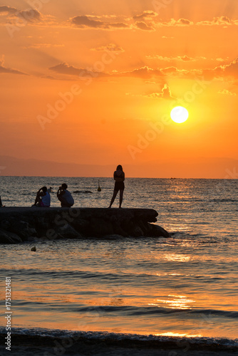Paralia, Katerini, Greece, 14.08.2025: Sunrise over the sea in Paralia, Katerini, Greece. Silhouettes of people and a girl standing against the sun.