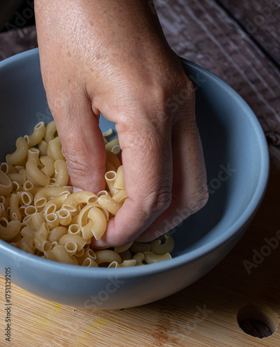 Manipulacion de alimentos, manejo de comida en la cocina, manos de mujer hispana mexicana agarrando pasta de coditos sin cocinar ,cruda, vista lateral