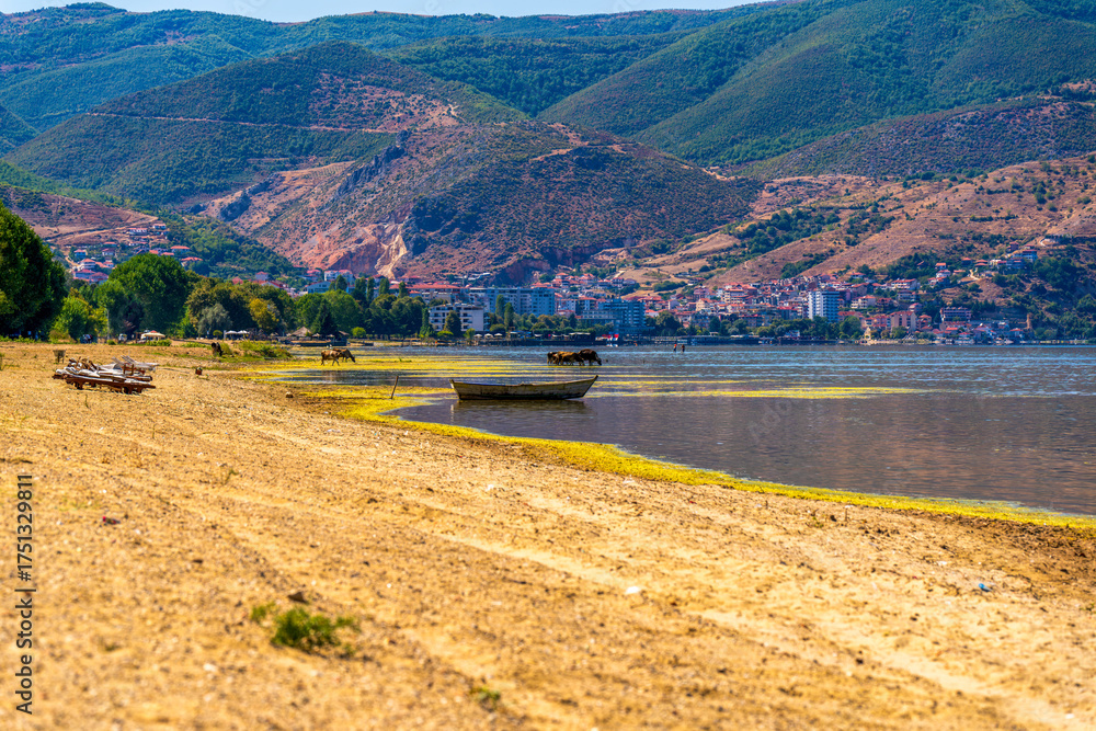 Naklejka premium Scenic view of Lake Ohrid near Pogradec, Albania with calm water, distant mountains, and a wooden boat under bright summer sunlight
