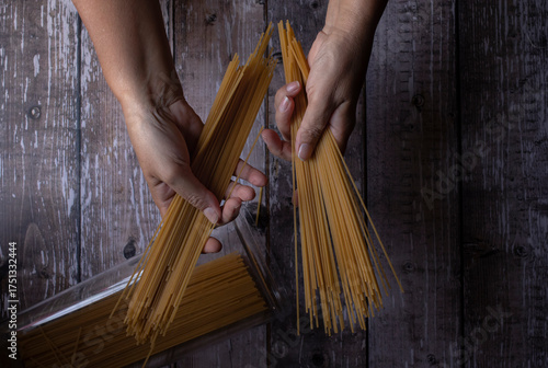 Manipulacion de alimentos, manejo de comida en la cocina, pasta italiana tomada con las manos de una mujer hispana mexicana sobre mesa de madera