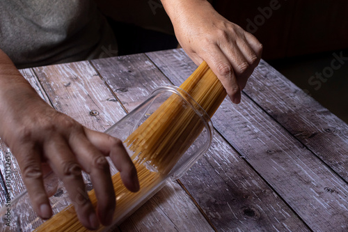Manipulacion de alimentos, manejo de comida en la cocina, manos guardando pasta  o espagueti en un contenedor de cristal sobre una mesa de madera