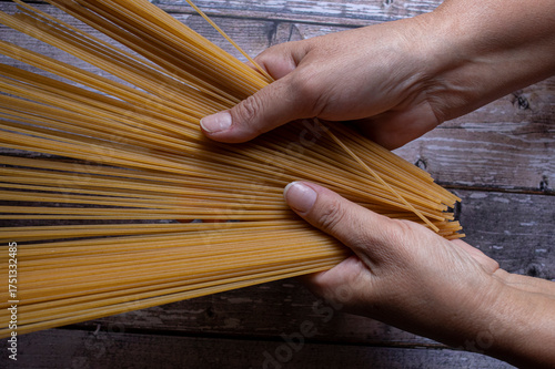 Manipulacion de alimentos, manejo de comida en la cocina, pasta italiana tomada con las manos de una mujer hispana mexicana sobre mesa de madera