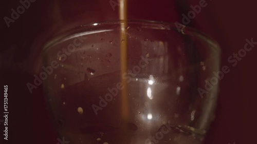 Coffee pours into transparent glass creating rich crema. Video footage of coffee streaming into a clear glass, forming a layer of crema.