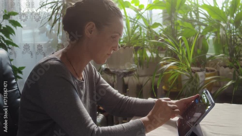 Woman interacting with tablet using stylus while sitting at desk in room