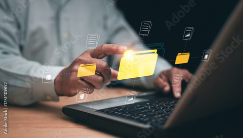 Digital document management concept. Businessman using laptop and touching virtual yellow folder icon and document icon on screen. Online data organization and modern information technology system.