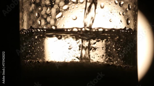 Pouring clear liquid into a glass with condensation, abstract view