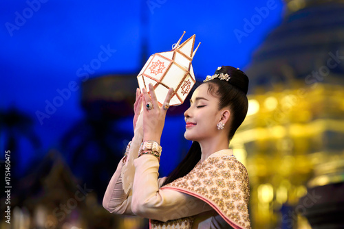 Pretty Asian woman in Thai traditional costume in the Hundred Thousand Lantern Festival or Yi Peng Festival for worship at Phra That Hariphunchai temple in Lamphun, Thailand.