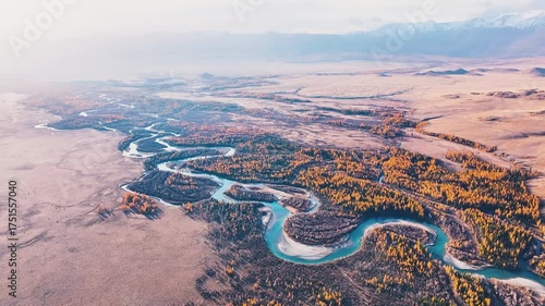 Witness the breathtaking beauty of Altai's nature, showcasing winding rivers and vibrant autumn foliage in a serene alpine valley amidst majestic mountains.