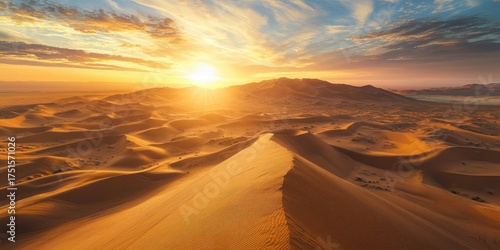 Fototapeta Naklejka Na Ścianę i Meble -  A vast, golden desert landscape with sand dunes stretching across the horizon under a dramatic, colorful sunset sky.