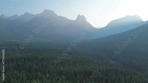 A cinematic drone flight over a remote mountain wilderness. The sun's first light creates a mystical glow and silhouettes the rugged peaks, painting a powerful and inspirational scene.