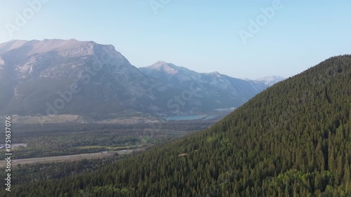 Cinematic drone video capturing the immense scale of a remote wilderness. The camera glides over the forest to reveal a grand valley and layered mountains on the horizon.