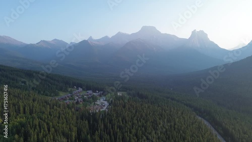 Cinematic aerial footage reveals a secluded village surrounded by wilderness. The rising sun casts a glow over the mountain peaks, creating a powerful and inspirational landscape.