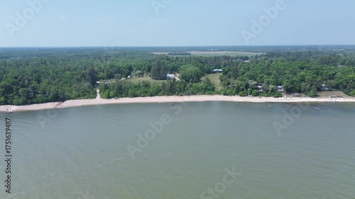This cinematic drone footage captures an expansive view of a large waterway and its undeveloped shoreline. The calm water reflects the sky, bordering the endless green forest on a summer day.