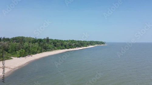 A smooth aerial flight over a serene, uninhabited coastline. The camera glides above the sandy shore where a lush green forest meets the calm sea, offering a perfect shot for travel or nature projects