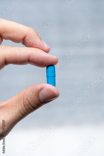 A hand holding multiple blue capsules hand holding one blue capsule between fingers