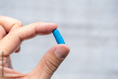 A hand holding multiple blue capsules hand holding one blue capsule between fingers
