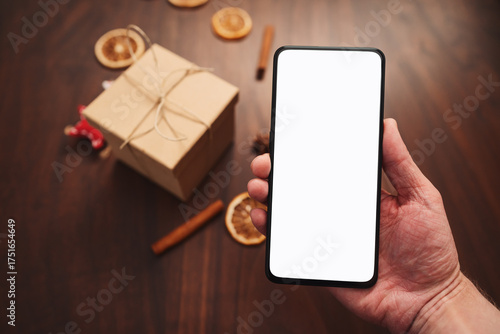 Man hand hold smarthone with white screen with christmas decorations on background
