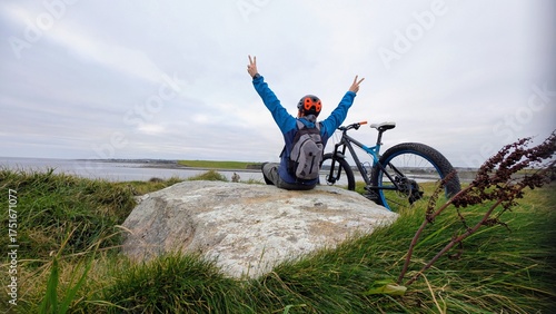 Adventure cyclist with mountain bike celebrating success on Wild Atlantic Way near Silverstrand Beach Galway, scenic Ireland coastline, freedom outdoor travel fitness lifestyle, exploration