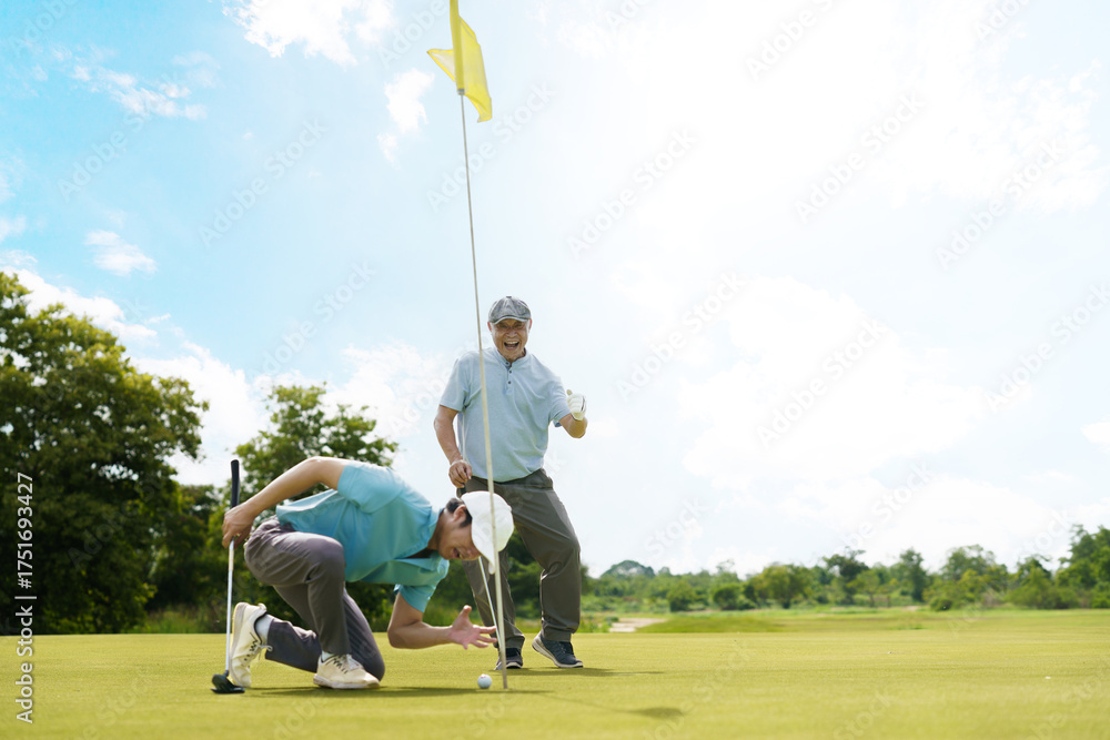 Obraz premium Asian golfer putting on green with senior cheering nearby.
