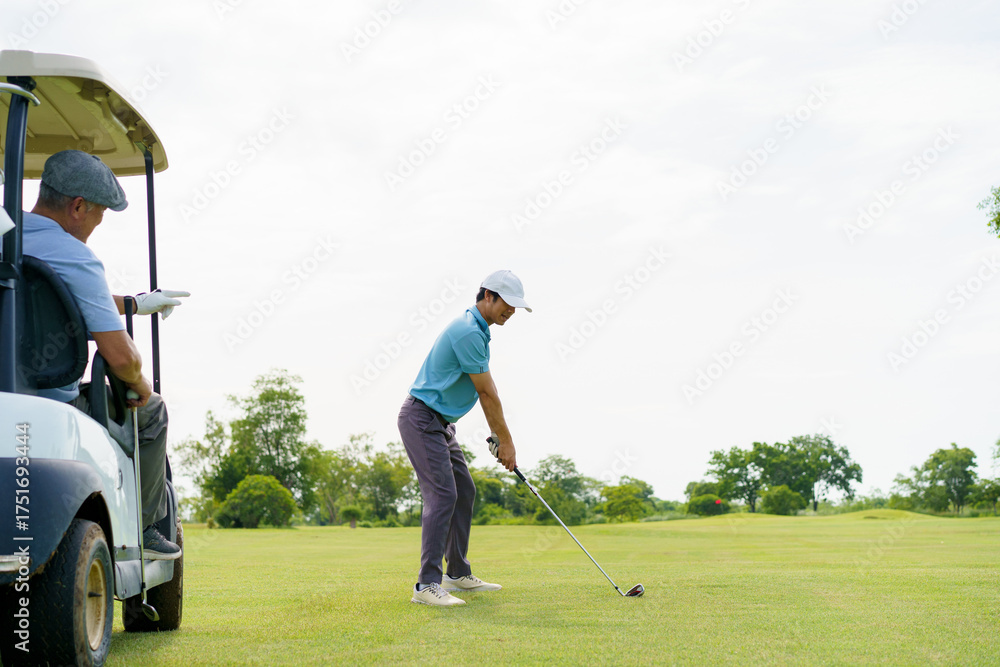Fototapeta premium Young Asian golfer hitting shot while senior watches from golf cart.