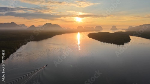 An aerial shot captures a serene landscape featuring a calm river meandering through lush vegetation. The setting sun casts a golden glow, creating a peaceful reflection on the water's surface.