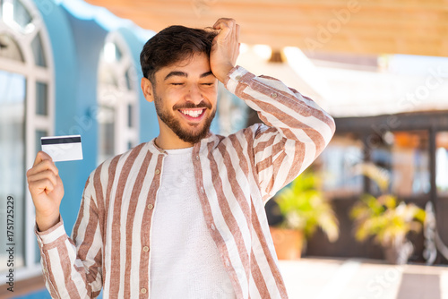 Handsome Arab man holding a credit card at outdoors has realized something and intending the solution