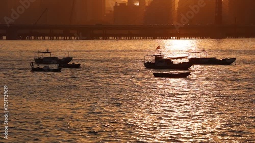 Scenic Qiantang River at sunset featuring bridge, city skyline, rolling waves, passing cars, boats, and sparkling water reflecting evening glow.
