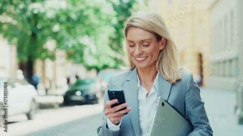 Smiling Businesswoman Checking Smartphone While Walking in City
