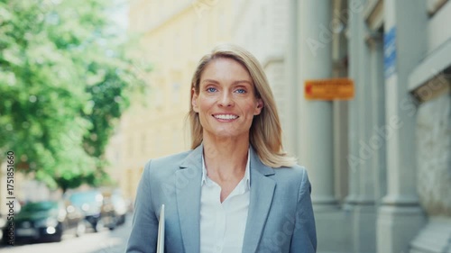 Smiling Businesswoman Walking Outdoors Holding Laptop in City