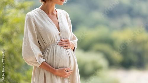 young pregnant woman in light cotton dress gently cradles her baby bump, surrounded by lush green background. scene conveys sense of anticipation and joy