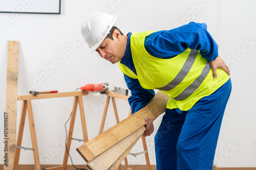 Photos Construction worker suffering back ache lifting work wooden slats on a house