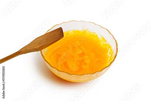 Closeup glass bowl with fresh homemade pumpkin puree and wooden spatula isolated on clean white background