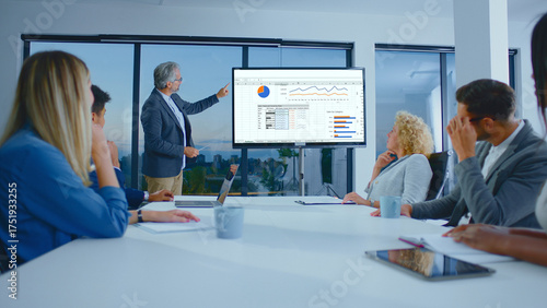 Foto Senior businessman presenting financial data and charts on a large screen to a d