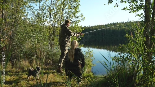 A man and a woman are fishing on the shore of a lake on a summer day. The man is casting a spinning rod into the lake. Fishing on the shore of a forest lake. Family fishing and outdoor recreation in