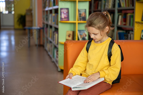 Portrait of a 7-8-year-old blonde girl in a yellow longsleeve in a library with books