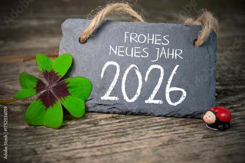 Wooden hang tag and slate with four leaf clover and sparklers with the german words for happy new year - frohes neues jahr 2026 on wooden weathered background