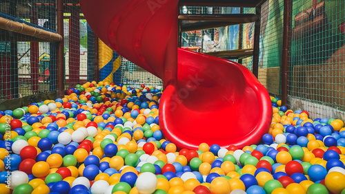 Obraz na plátně Bright red spiral slide ending in colorful ball pit inside indoor playground, fi