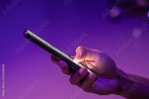 A man scrolling on social media apps or searching for information online on his smartphone on blue and purple neon lights background