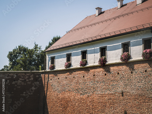 The outer façade of Stari Grad Castle in Cakovec, Croatia, with its red brick walls and white upper structure. Flower-adorned windows add charm to the historic Renaissance architecture.