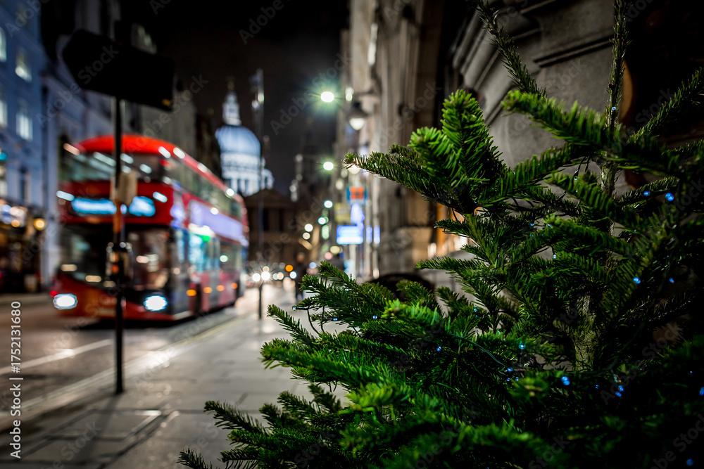 Naklejka premium Classic red double-decker bus on festive London street at night