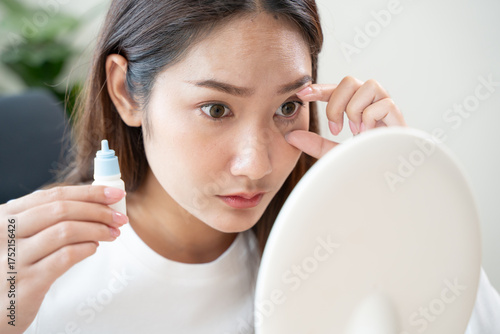 asian young woman using medical eye drops to treat dry eye and irritation.