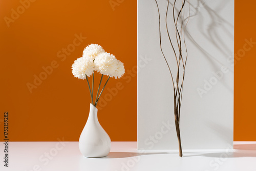 Flores de crisantemo blancas decorativas en un jarrón blanco sobre fondo naranja	