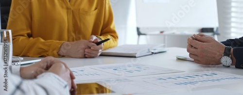 Business professionals gathered around conference table, reviewing financial charts, collaborating on strategic planning and corporate analysis
