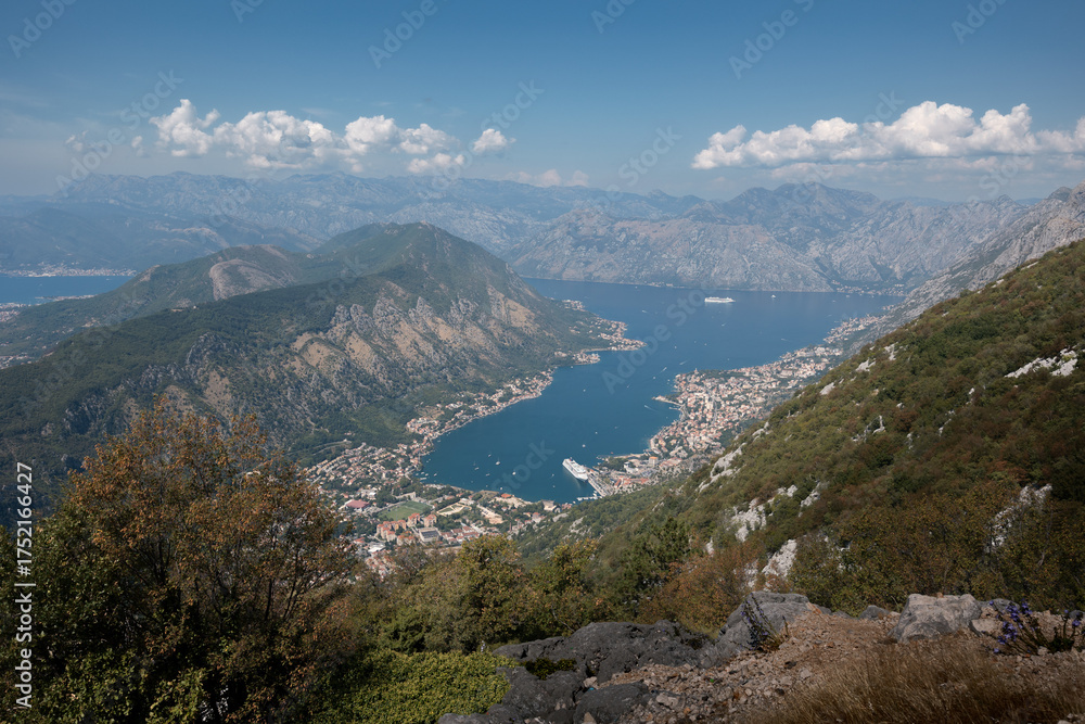 Obraz premium Kotor bay azure water surrounded by rocky mountains and towns along shore on sunny day, Montenegro