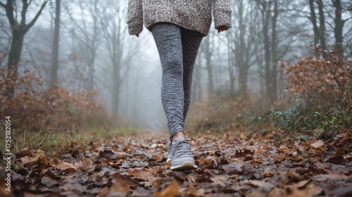 woman walking along a leaf-strewn forest path in autumn mist, casual gray athletic leggings and sweater, serene nature scene 