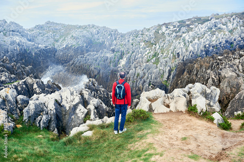 A man in a red jacket looks at the cliffs in a karst area where the waves of the sea reach