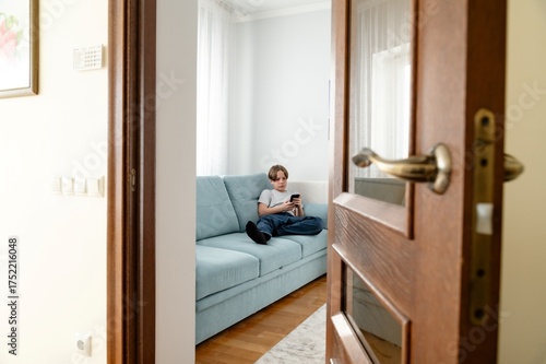 Teen using smartphone while relaxing on sofa in cozy living room during the afternoon