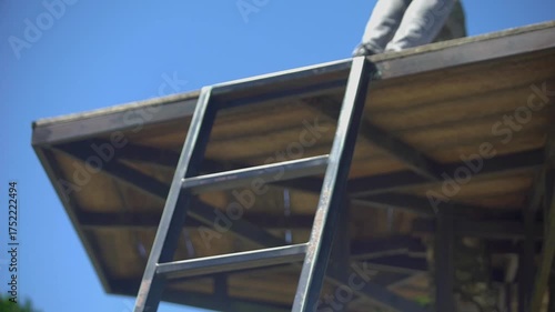 Man in plaid shirt and jeans climbing a ladder outdoors on a sunny day.