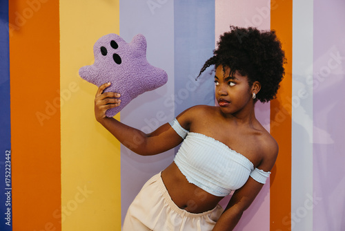 Young Black woman holding a plush ghost toy in colorful Halloween-themed space